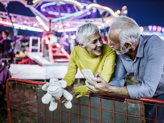 Senioriges Paar auf Jahrmarkt schaut sich lächelnd an.