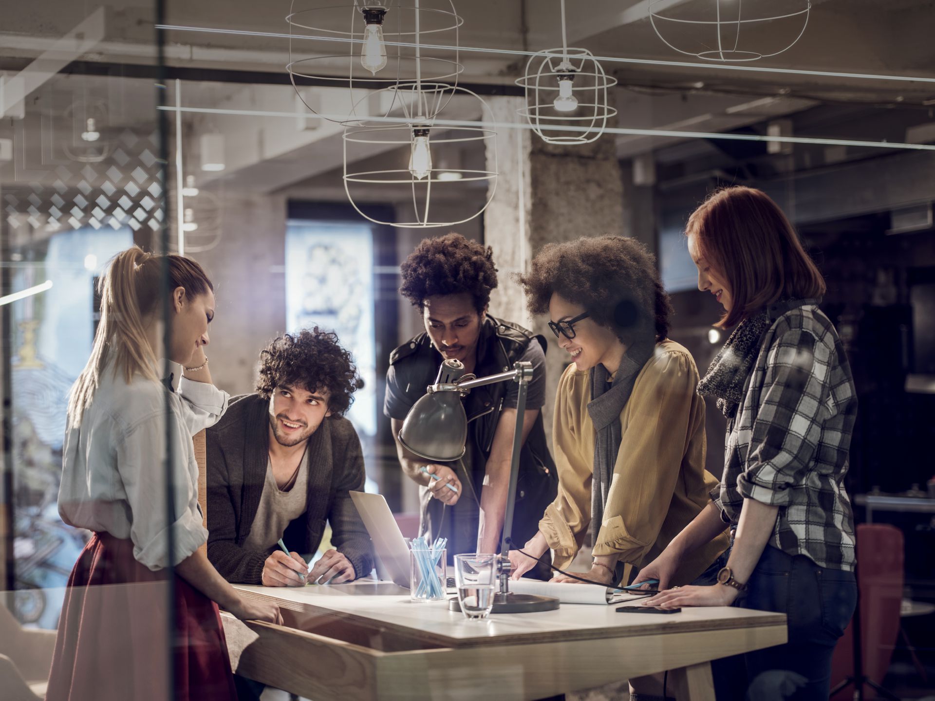 Diverses Team steht um Tisch und brainstormen zusammen. 