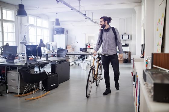 Junger Mann läuft entspannt mit Fahrrad durchs Büro