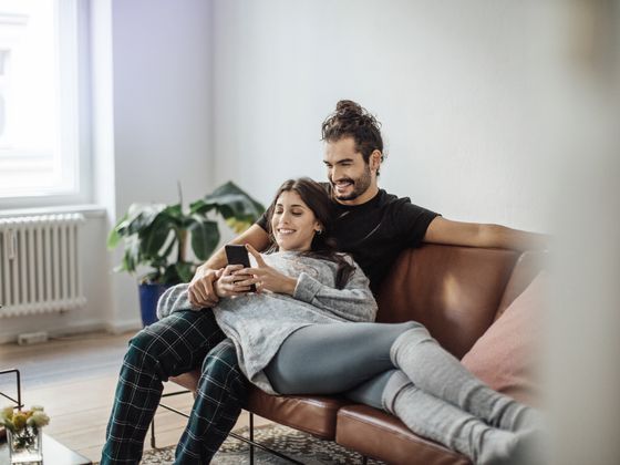 Ein Paar sitzt auf der Couch und schau gemeinsam aufs Handy.